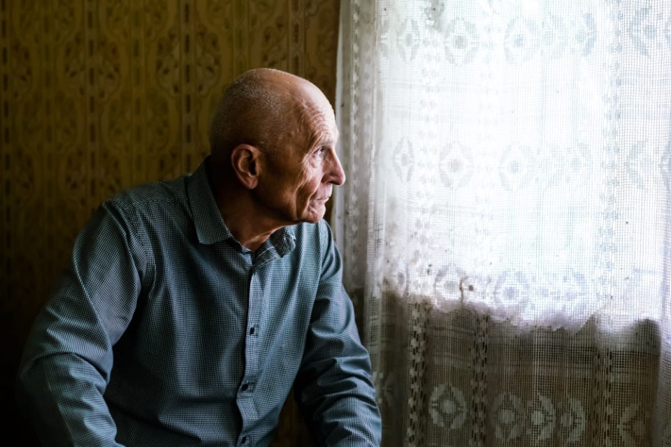 A senior man sits at a window after getting government assistance for assisted living.